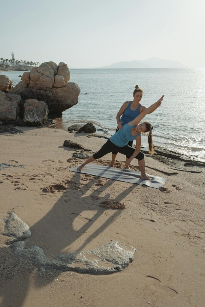 Two women practicing yoga by the sea, enhancing fitness and relaxation.
