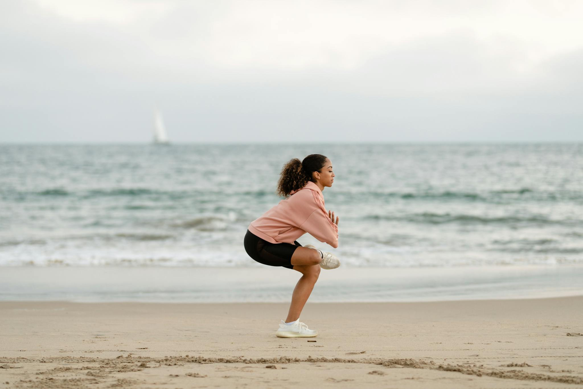 Woman performing yoga on a serene beach with ocean waves in the background.